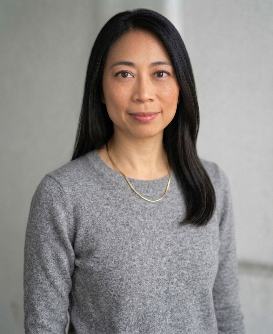 Professional headshot of Asian woman with long black hair wearing gray sweater and gold necklace.
