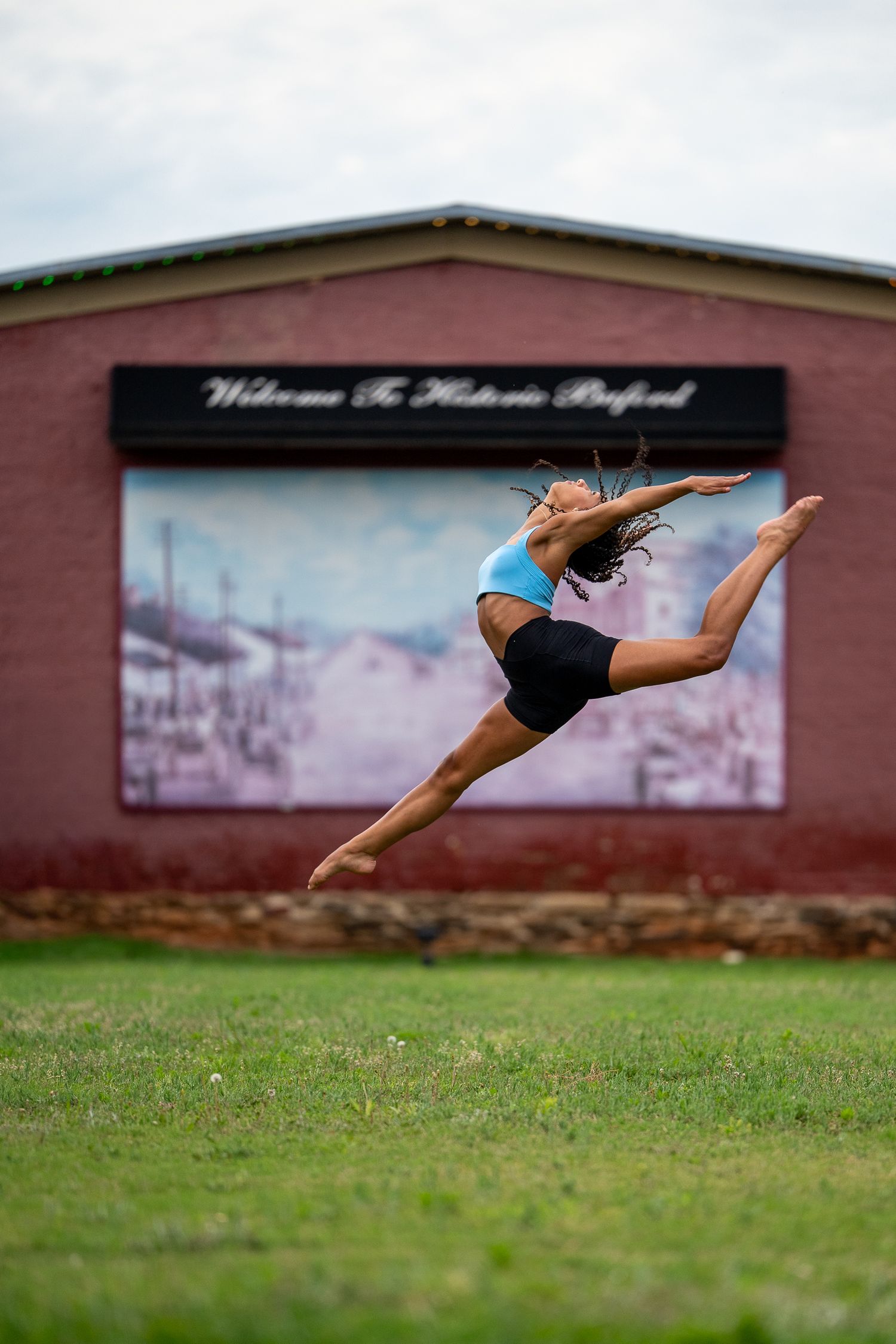 Female dancer performs aerial split jump in front of historic Oxford building.