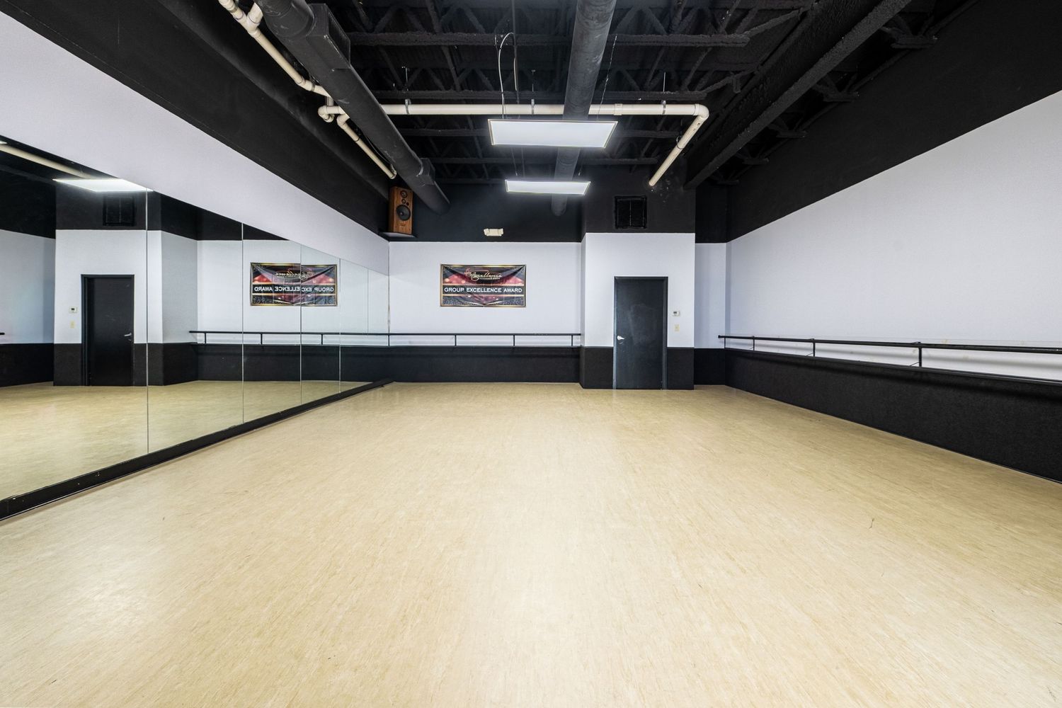 Spacious dance studio with hardwood floors, mirrored walls, ballet barres, and bright overhead lighting.