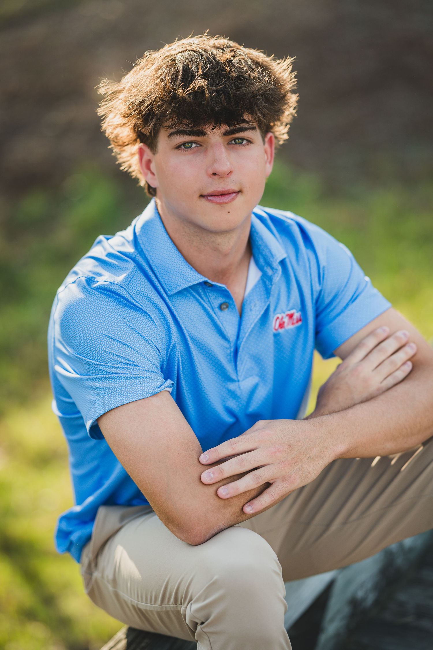 Teenage boy in light blue polo shirt sitting outdoors for senior portrait photo session.