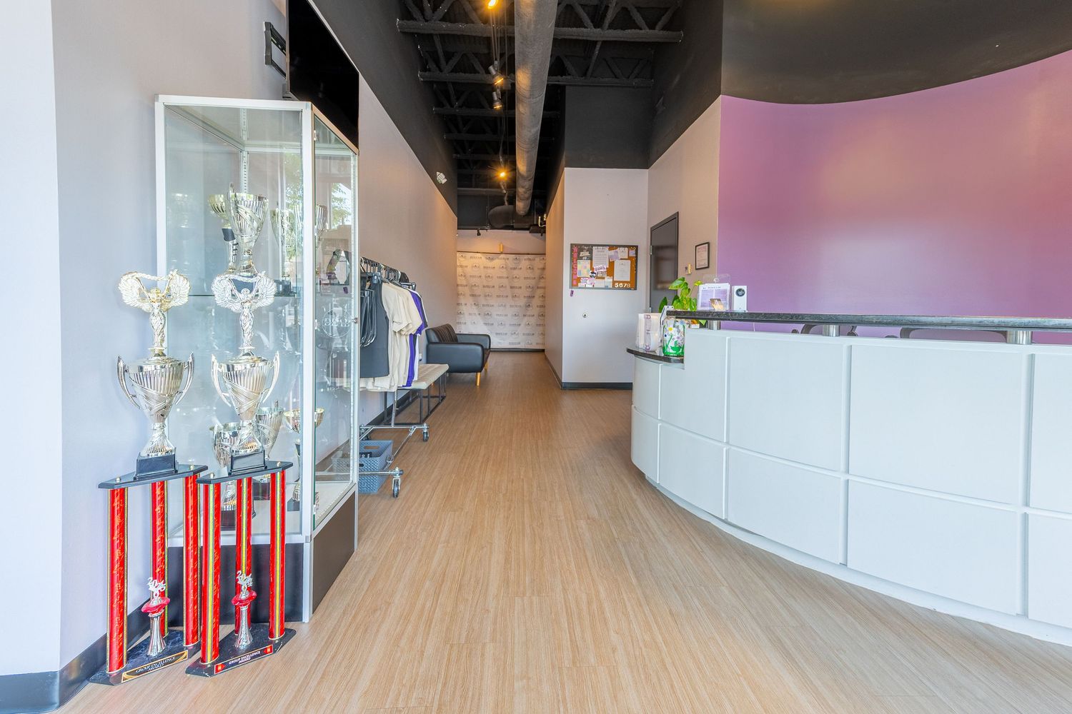 Modern reception area with trophy display case, hardwood floors, purple accent wall, and white curved front desk.