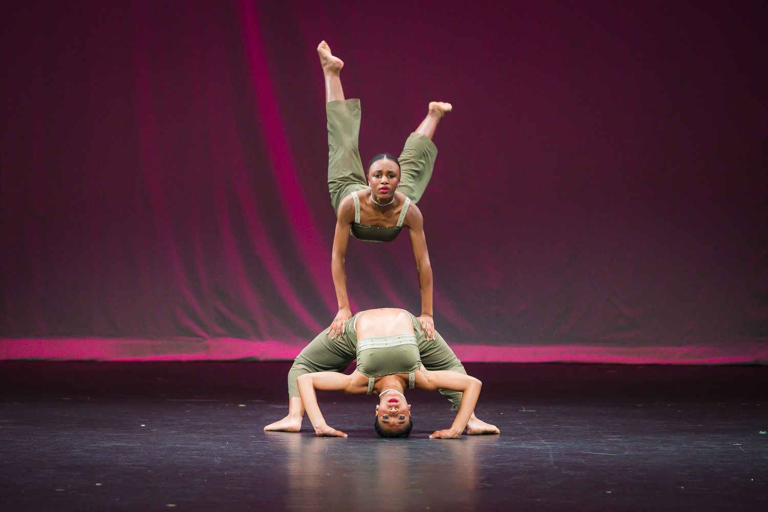 Two acrobatic dancers perform a stunning balancing act on stage wearing matching green costumes.