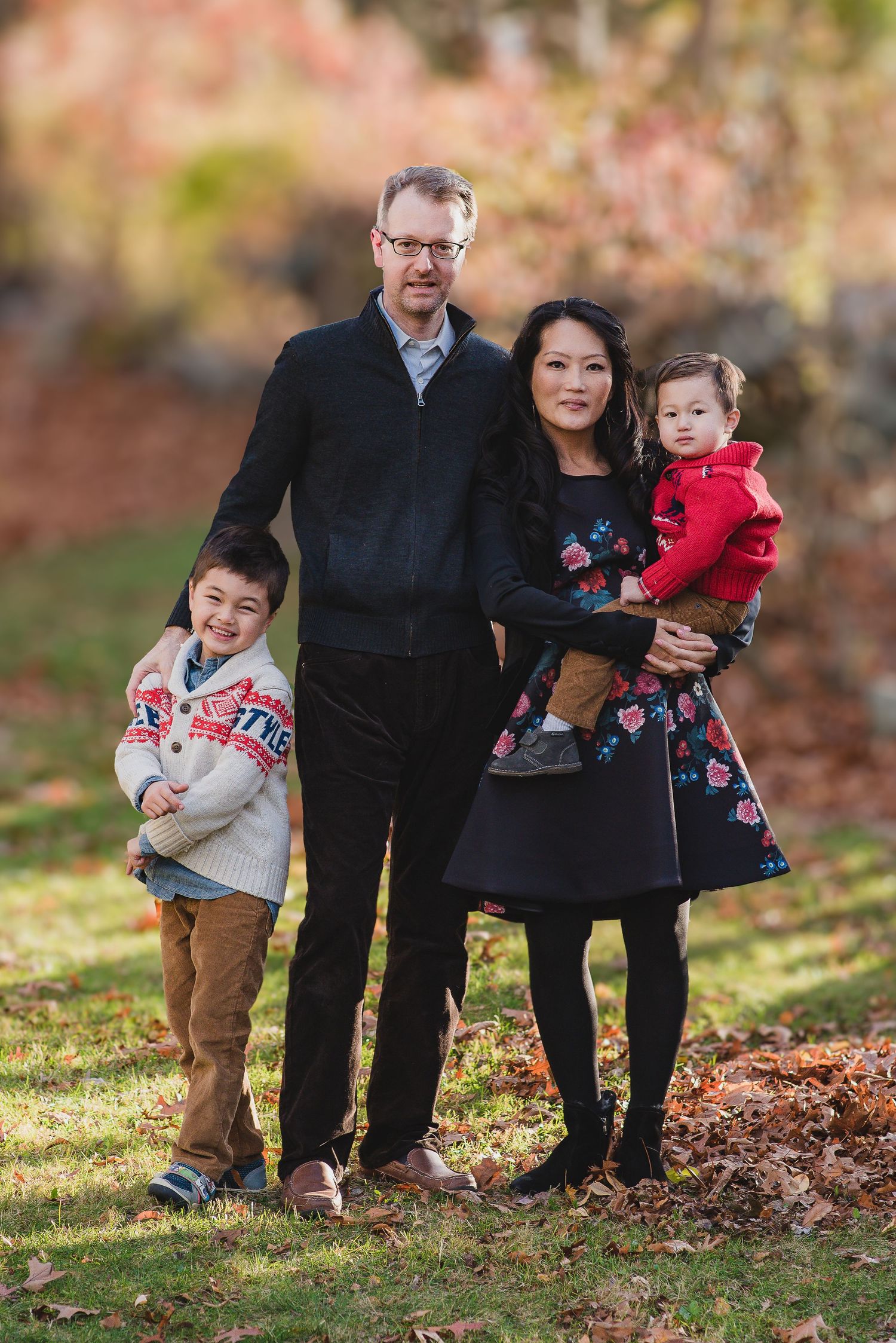 Family of four posing outdoors in autumn park with colorful fall foliage.