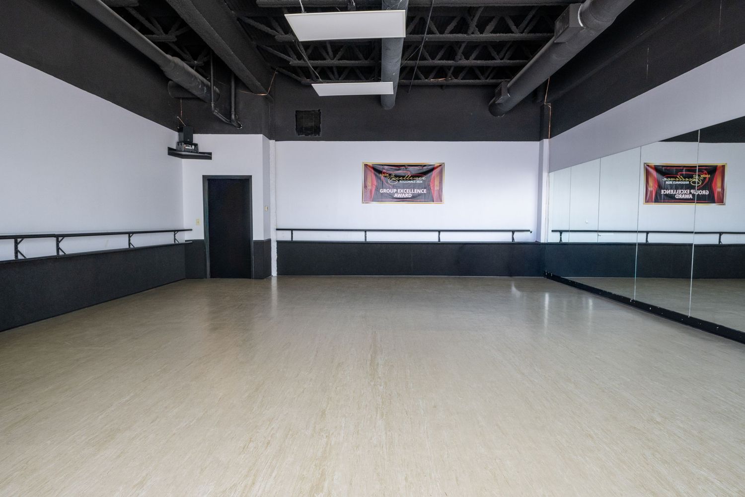 Spacious dance studio with mirrored walls, ballet barres, and polished hardwood floors under bright overhead lighting.
