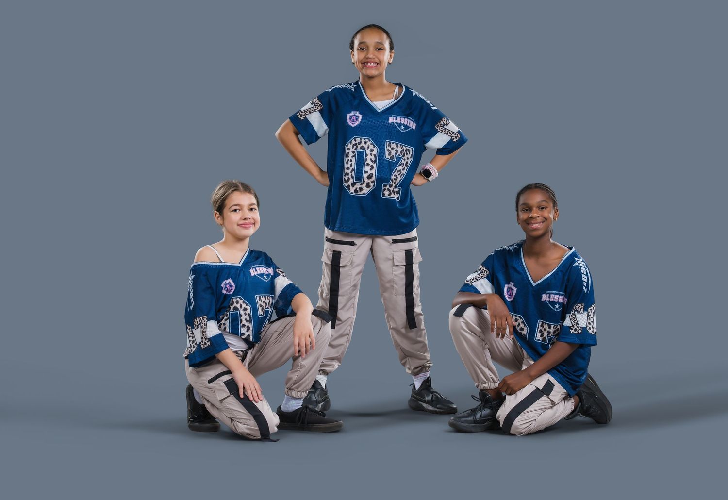 Three youth hip-hop dancers pose in blue number 07 jerseys against a gray studio background.