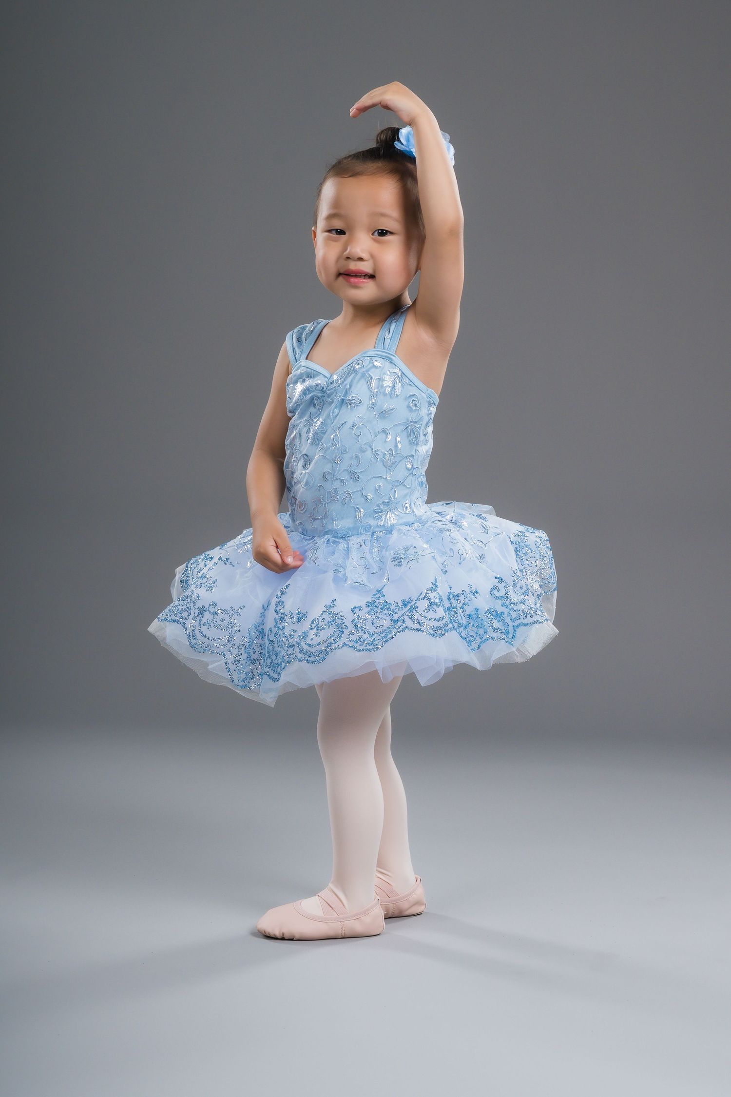 Young Asian girl in blue tutu ballet dress performing classical ballet pose in studio.
