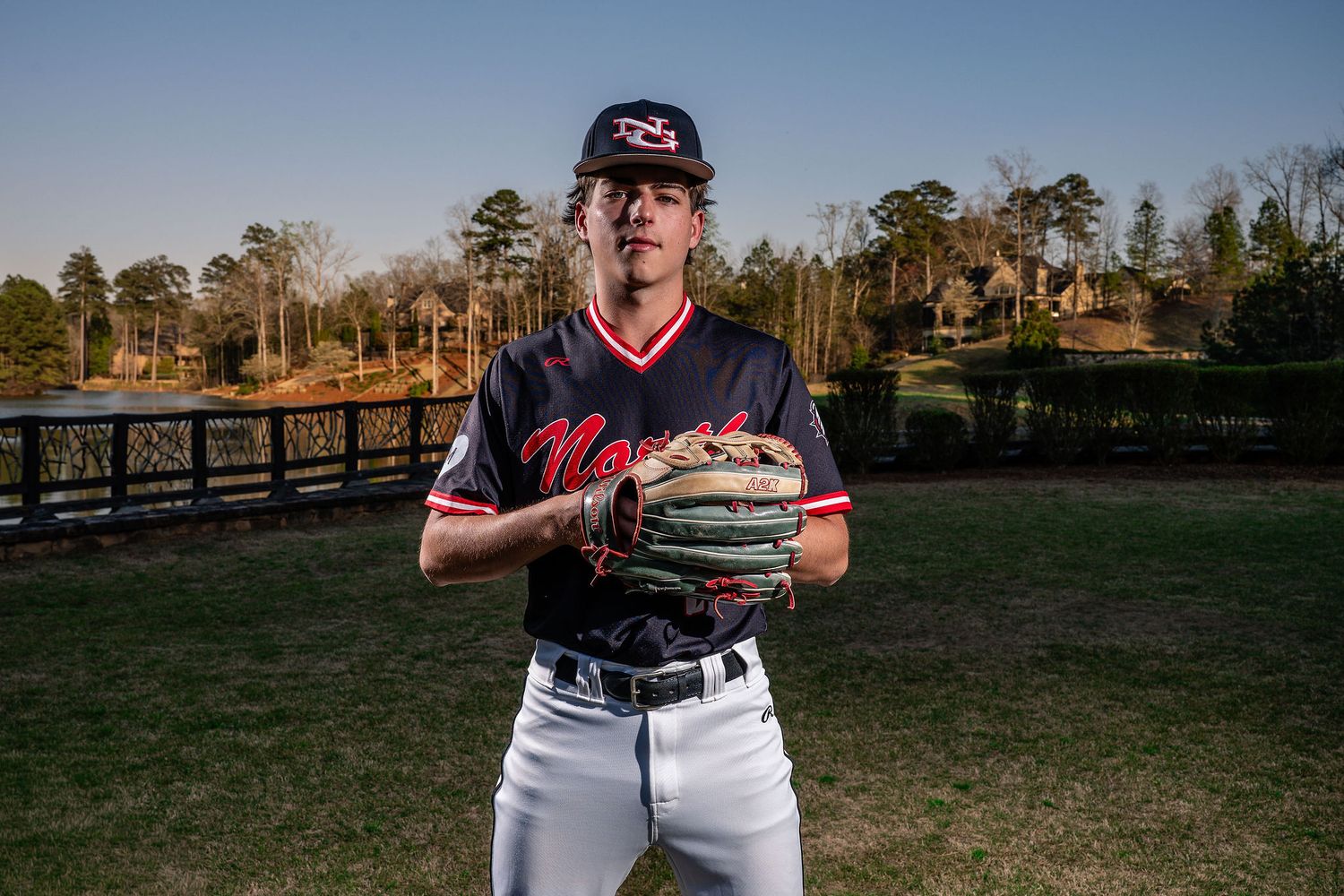 Young baseball pitcher in navy North uniform holds glove on green field outdoors.