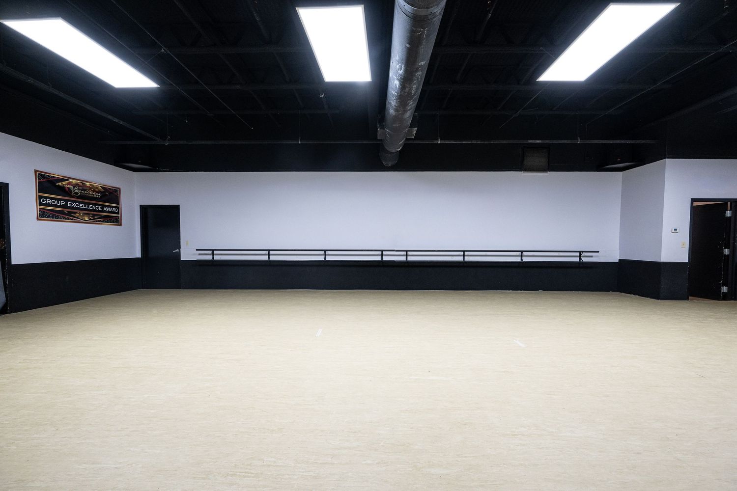Spacious dance studio with ballet barres, white walls, beige flooring, and bright overhead lighting.