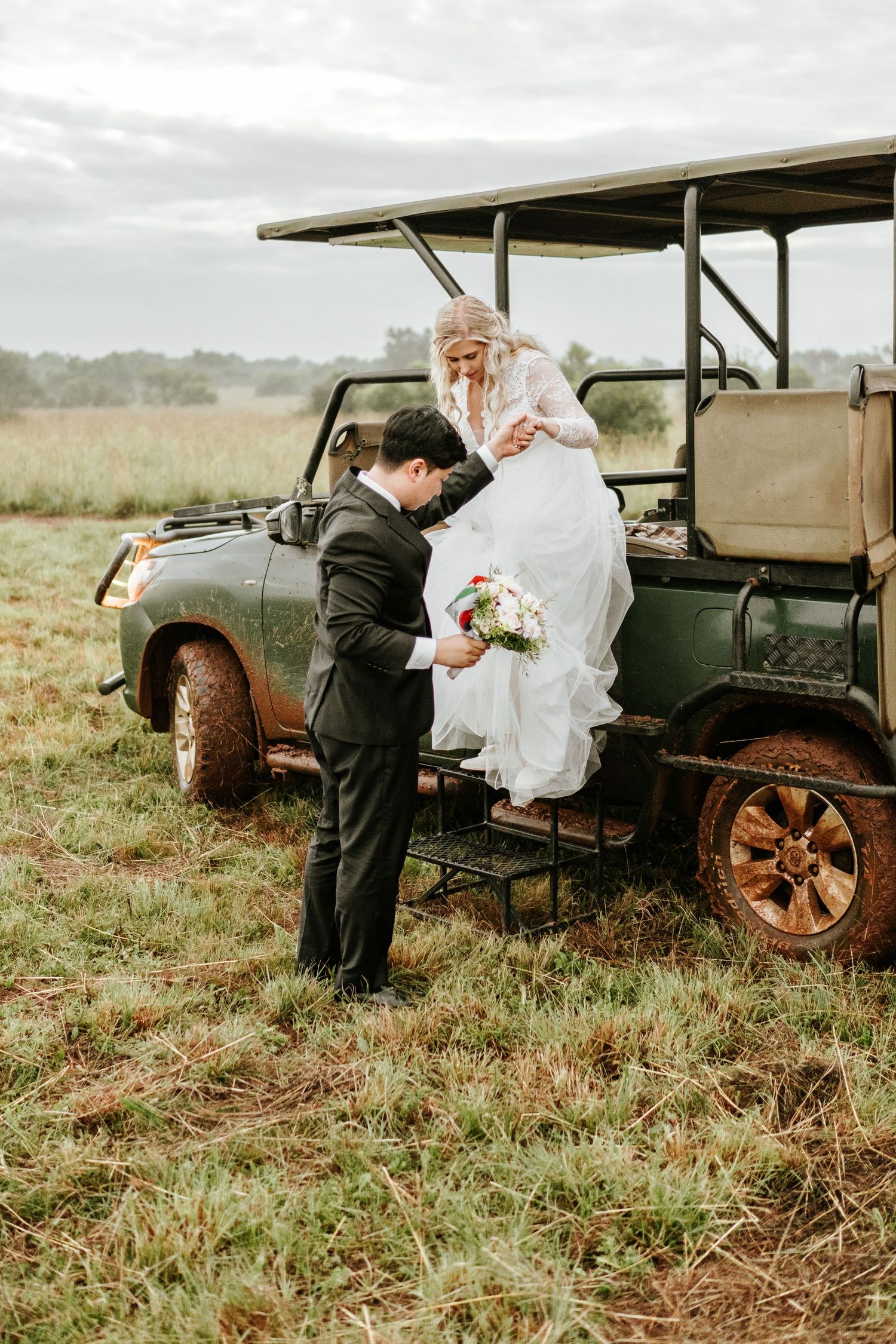 Groom helping bride descend from a rustic safari vehicle in a lush field on their wedding day photographed by Laughing Lamp Photo & Film