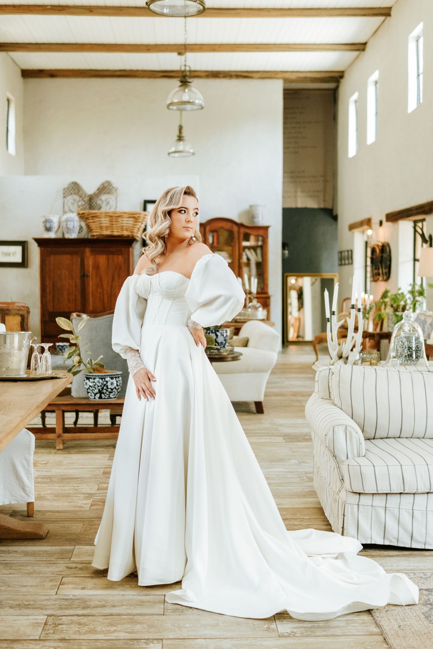 Stunning bride in a white ballgown with puff sleeves posing in a rustic farmhouse interior.