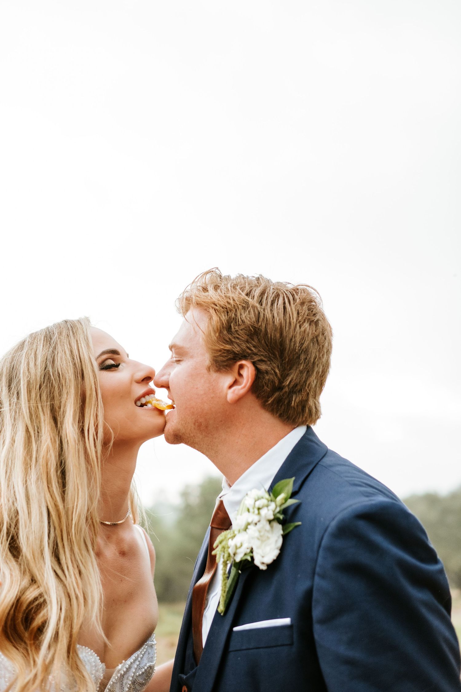 Bride and groom sharing a playful kiss while eating at their outdoor wedding celebration.