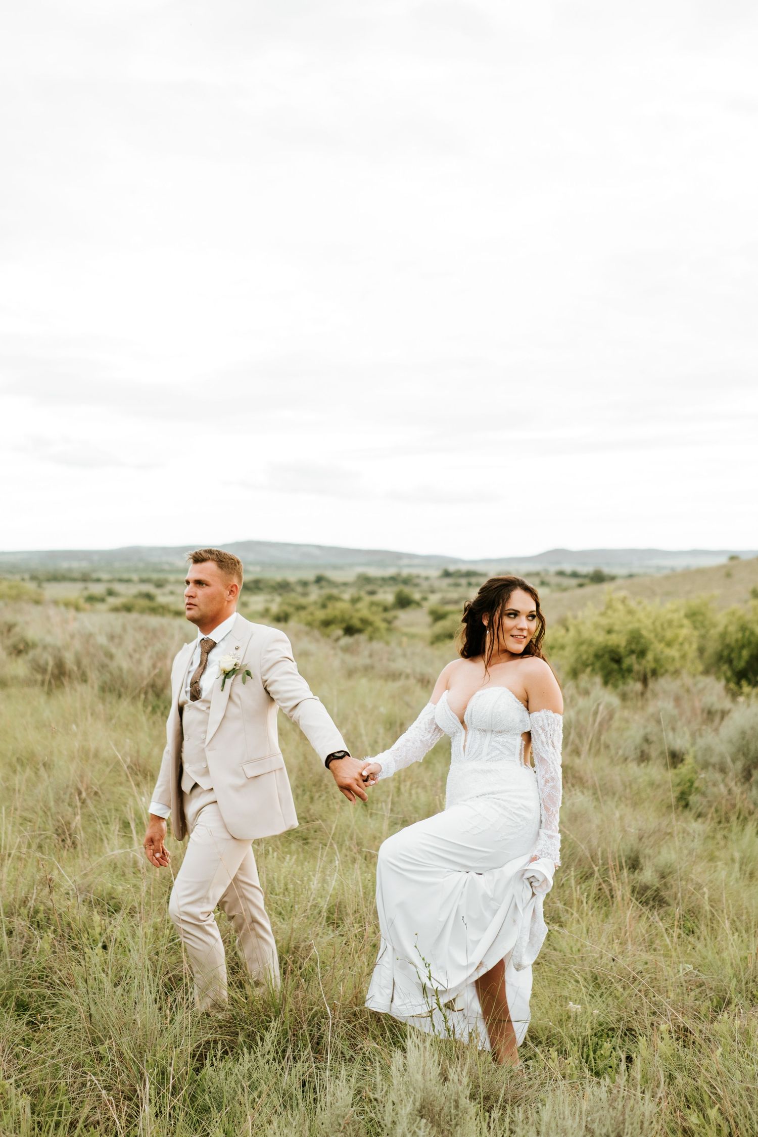 Bride and groom walking hand in hand through a lush green field at their outdoor wedding.
