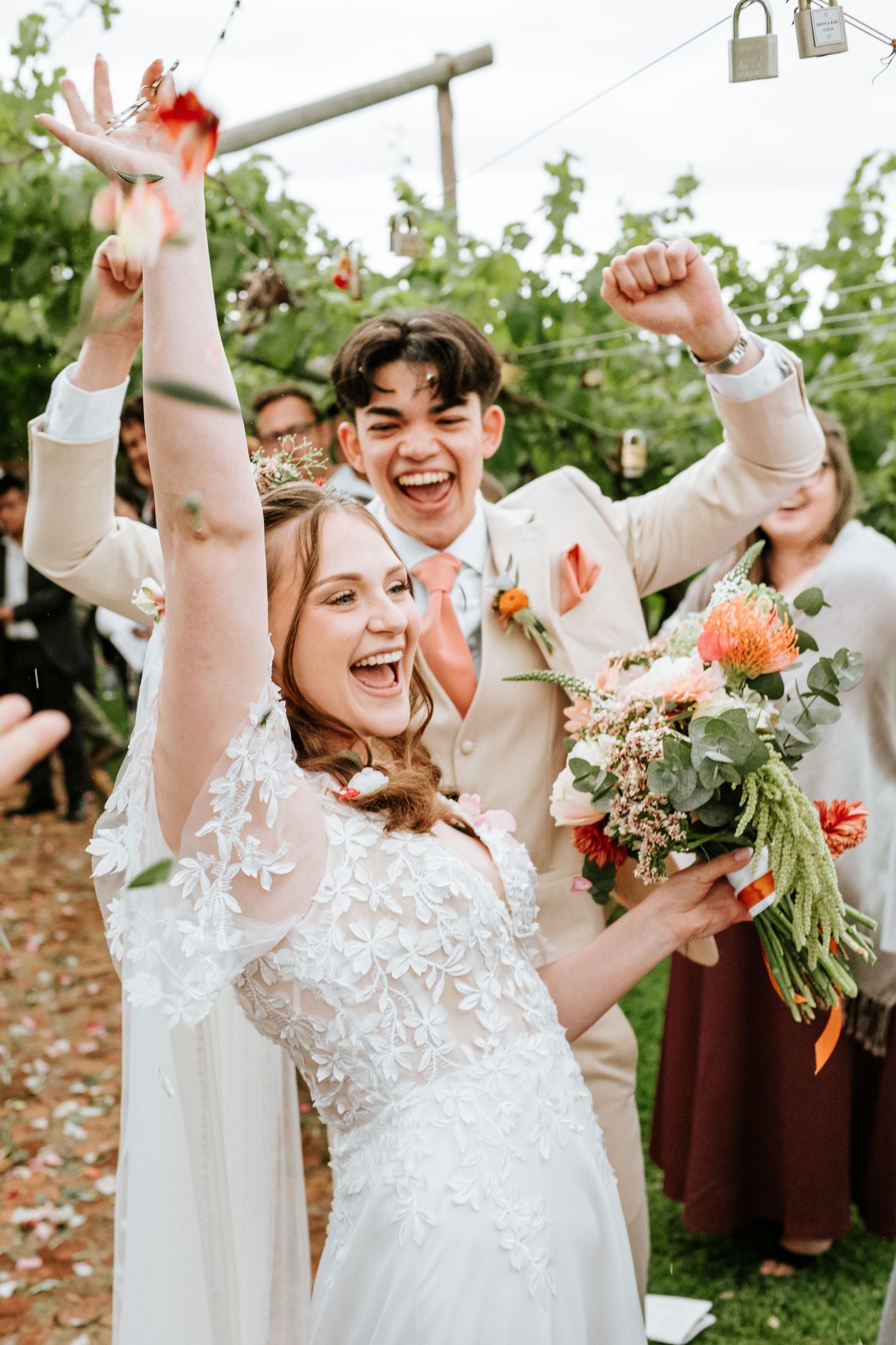 Ecstatic bride and groom celebrating with confetti, bride holding colorful bouquet at outdoor wedding reception.