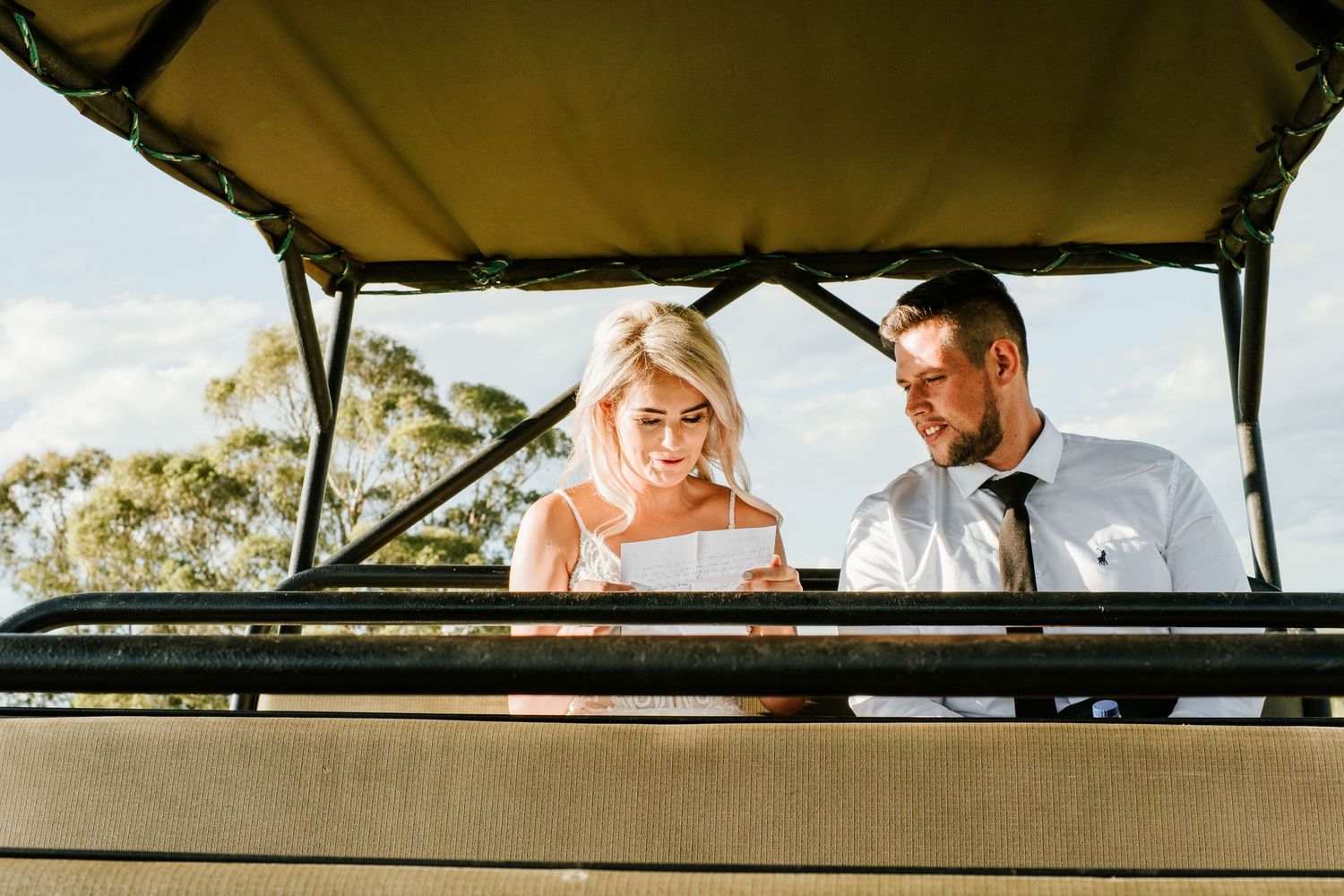 Smiling bride and groom sitting together in an safari vehicle, sharing a joyful moment outdoors.