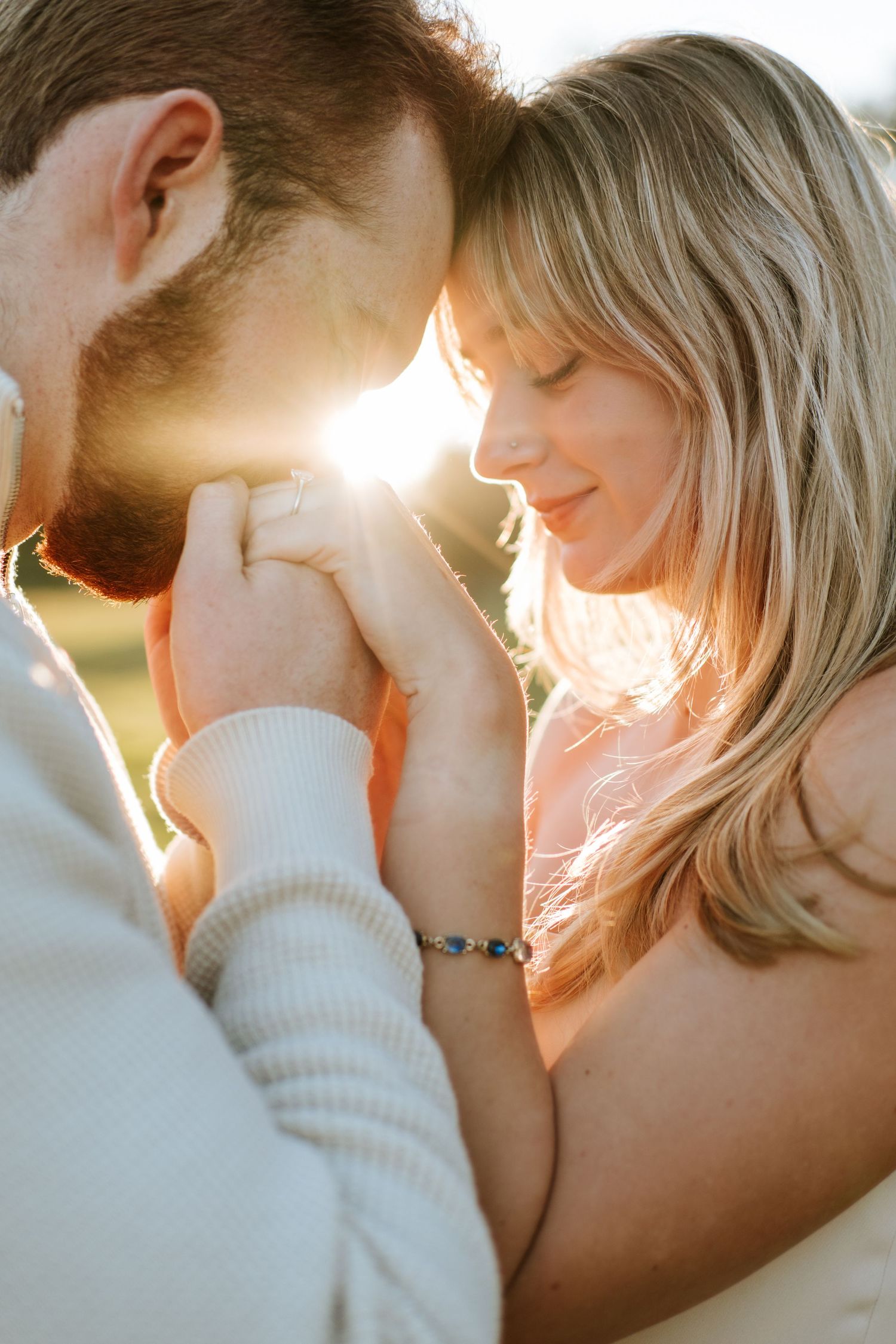 Close-up of couple holding hands forehead-to-forehead with golden sunlight glowing between them.