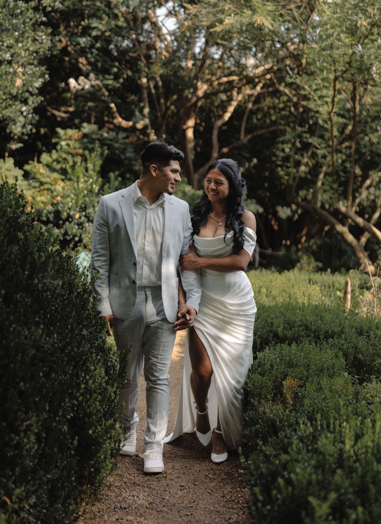 Engaged couple walking hand in hand through a lush garden