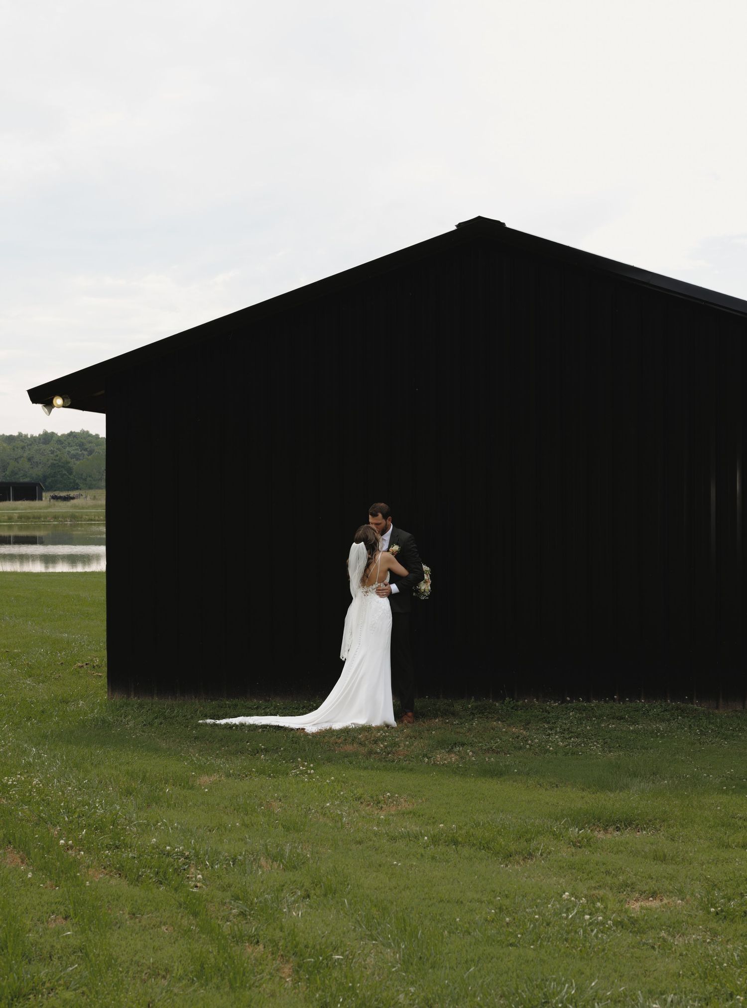 Bride and groom embracing beside a dark barn on their wedding day