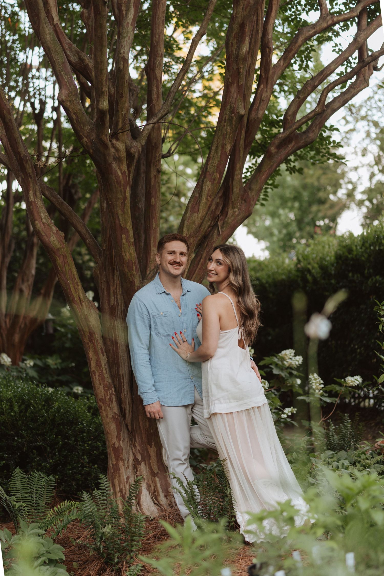 couple standing together beneath a large tree during an outdoor portrait session