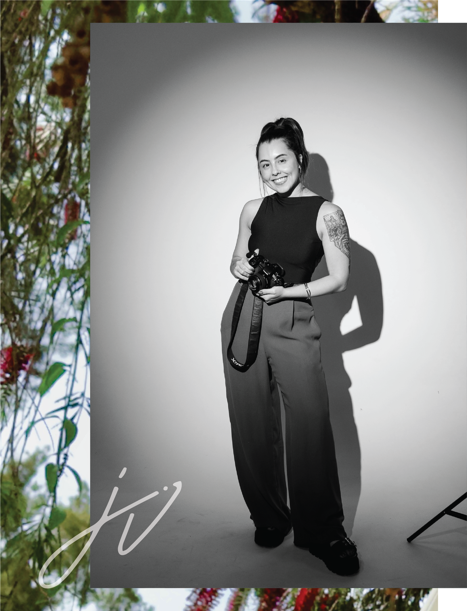 Female wedding photographer smiling and holding a camera in a black and white portrait.