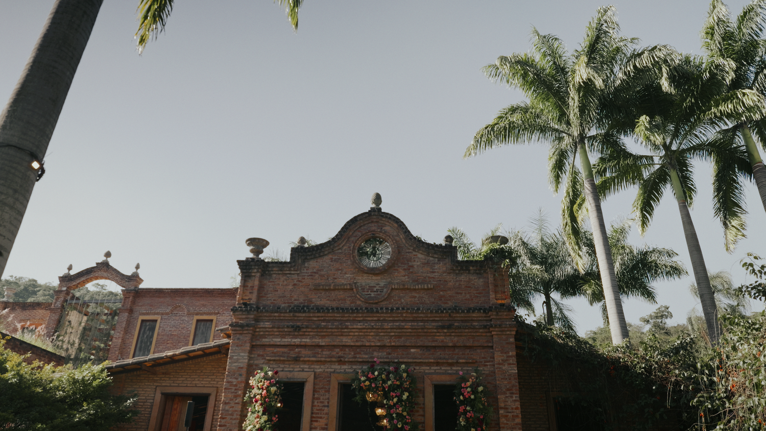 Charming brick building with palm trees and floral decorations at a wedding venue.