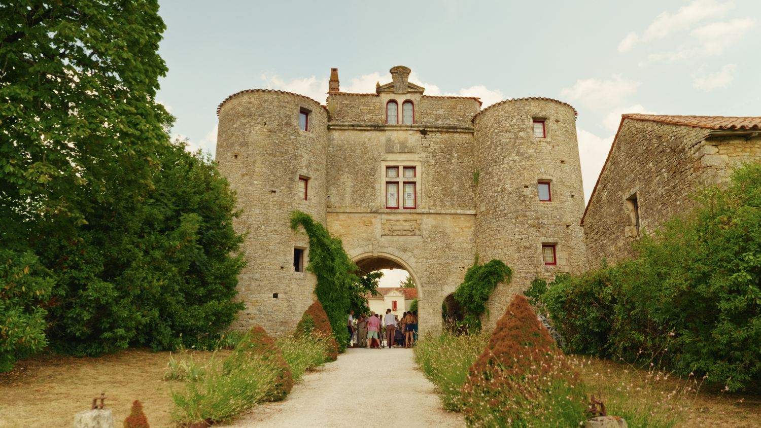 Historic stone castle entrance with an arched gateway surrounded by lush greenery.