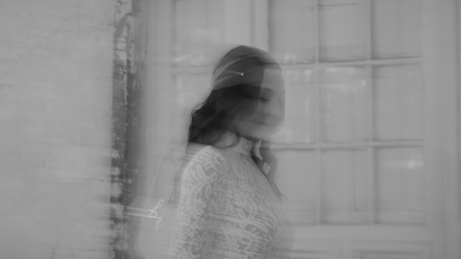 Artistic black and white double exposure of a bride in a lace gown near a window.