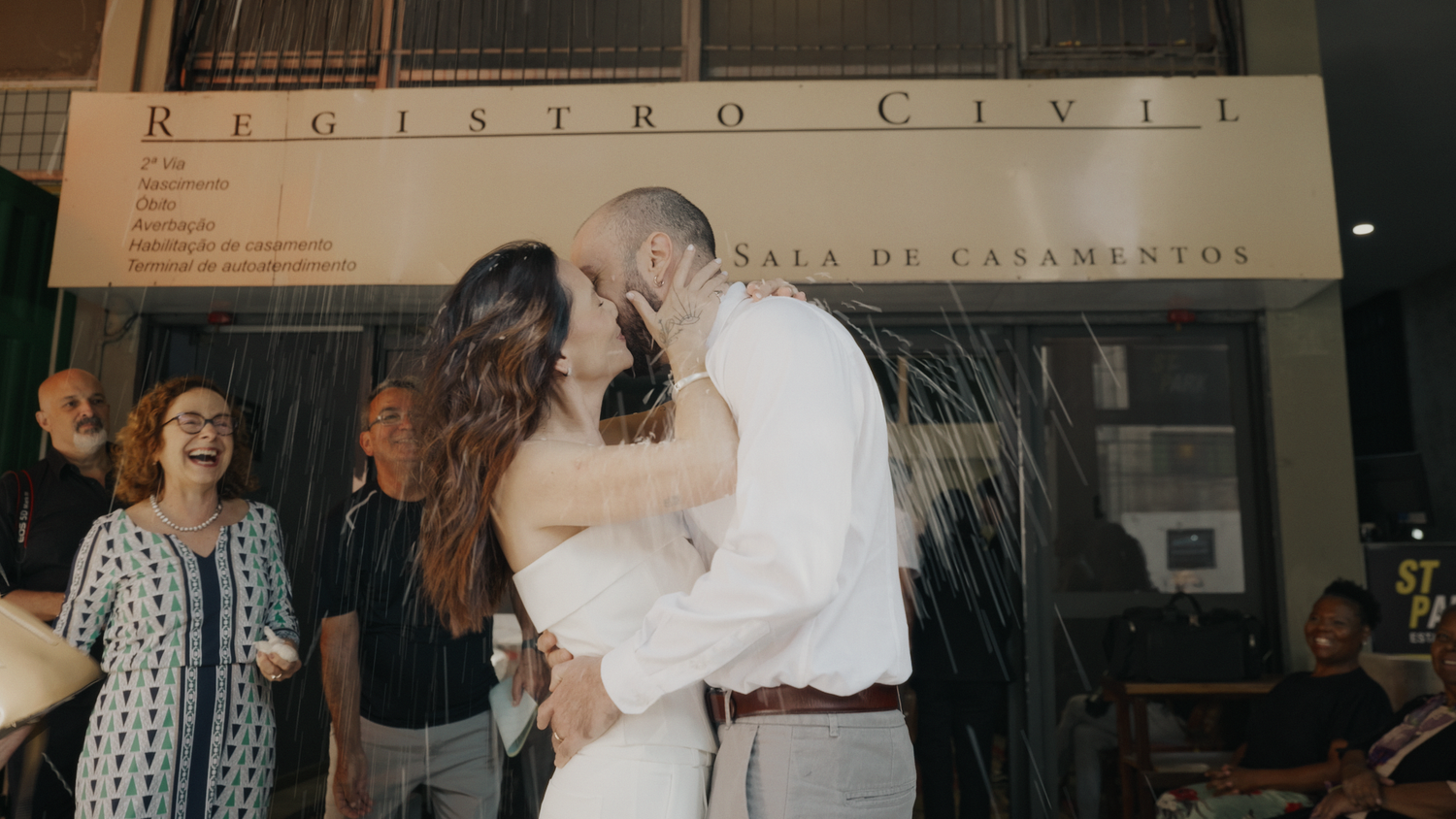 Newlyweds share a kiss outside Registro Civil marriage hall with celebrating guests around them.