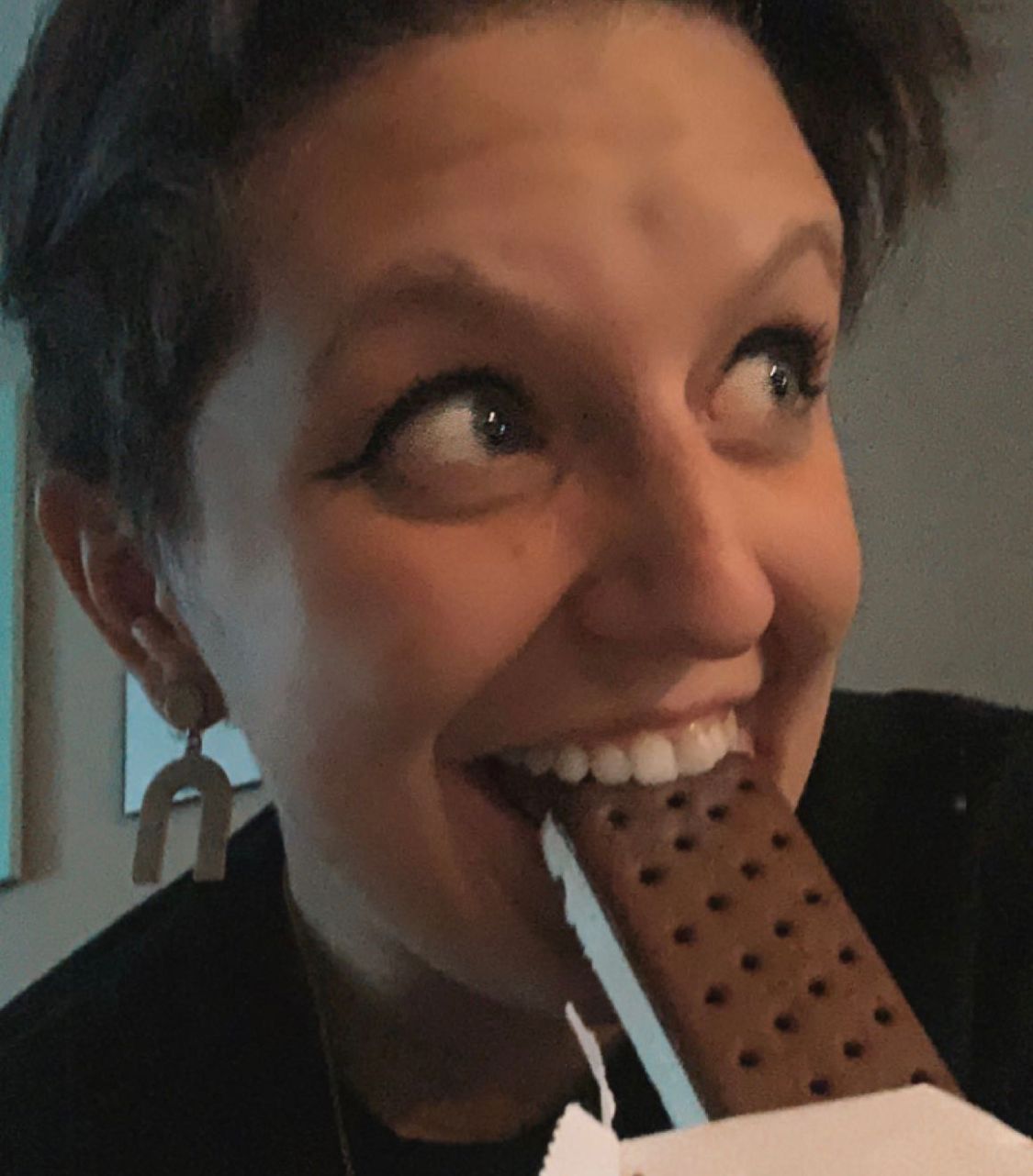 Woman excitedly biting into a large chocolate ice cream bar.