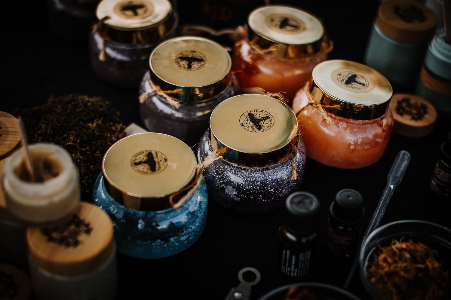 Assorted colorful glass jars filled with loose leaf teas and spices on a dark market table.