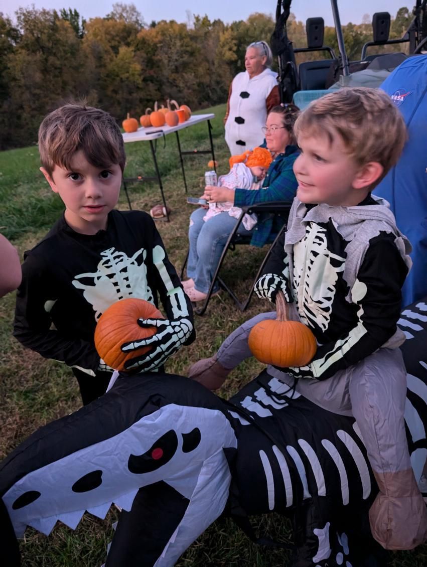 Two boys in skeleton Halloween costumes holding pumpkins at fall harvest event.
