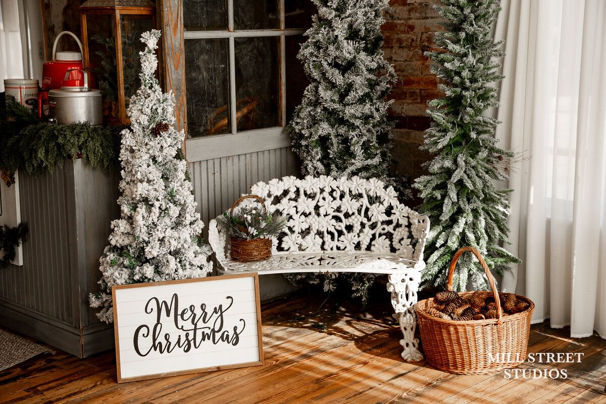 White ornate bench with flocked Christmas trees and Merry Christmas sign in festive holiday porch display.