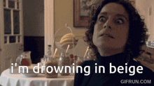 A woman sitting at a table with text overlay reading I'm drowning in beige in a humorous GIF.