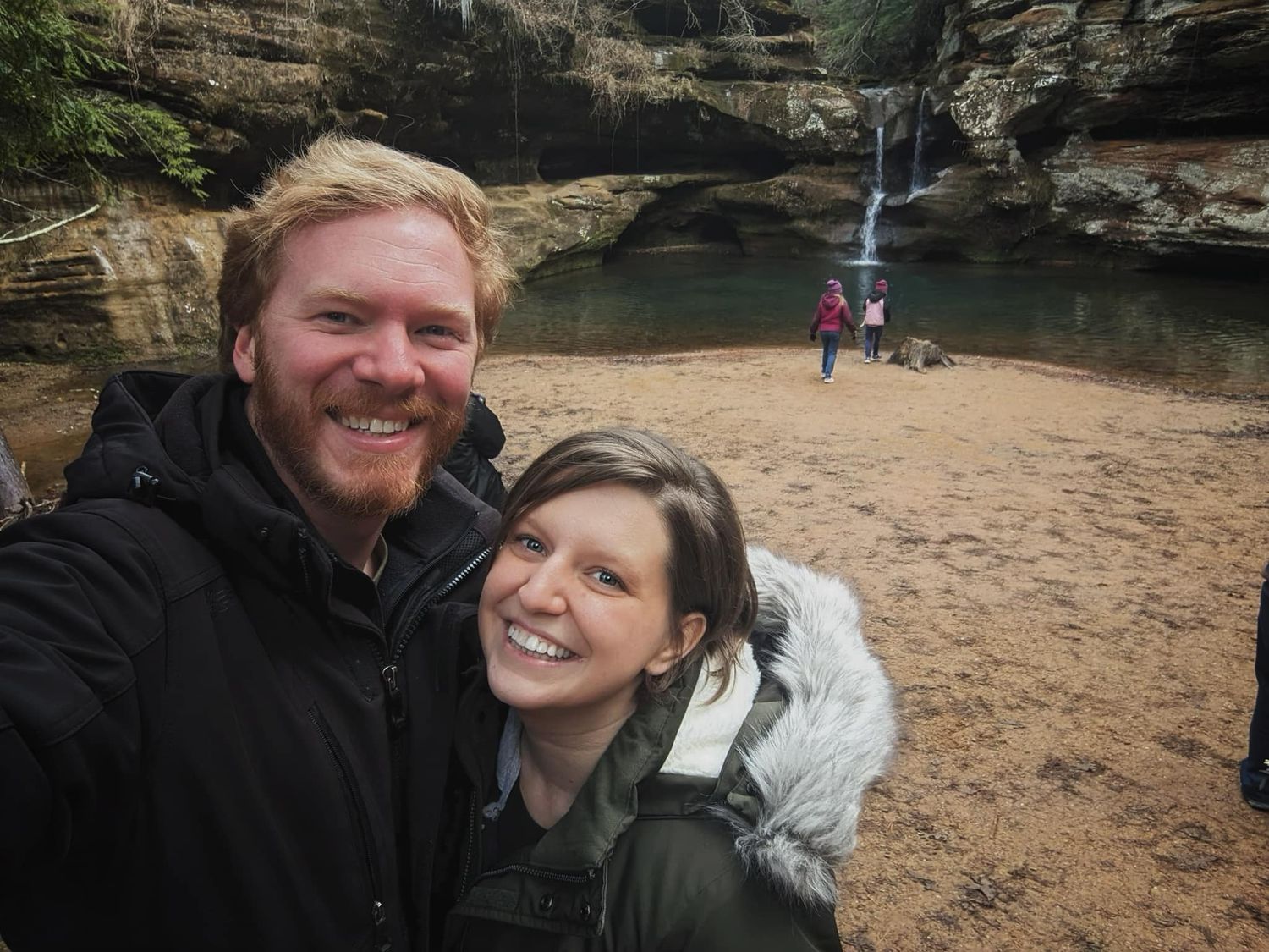Couple smiling in selfie near waterfall in rocky canyon landscape.
