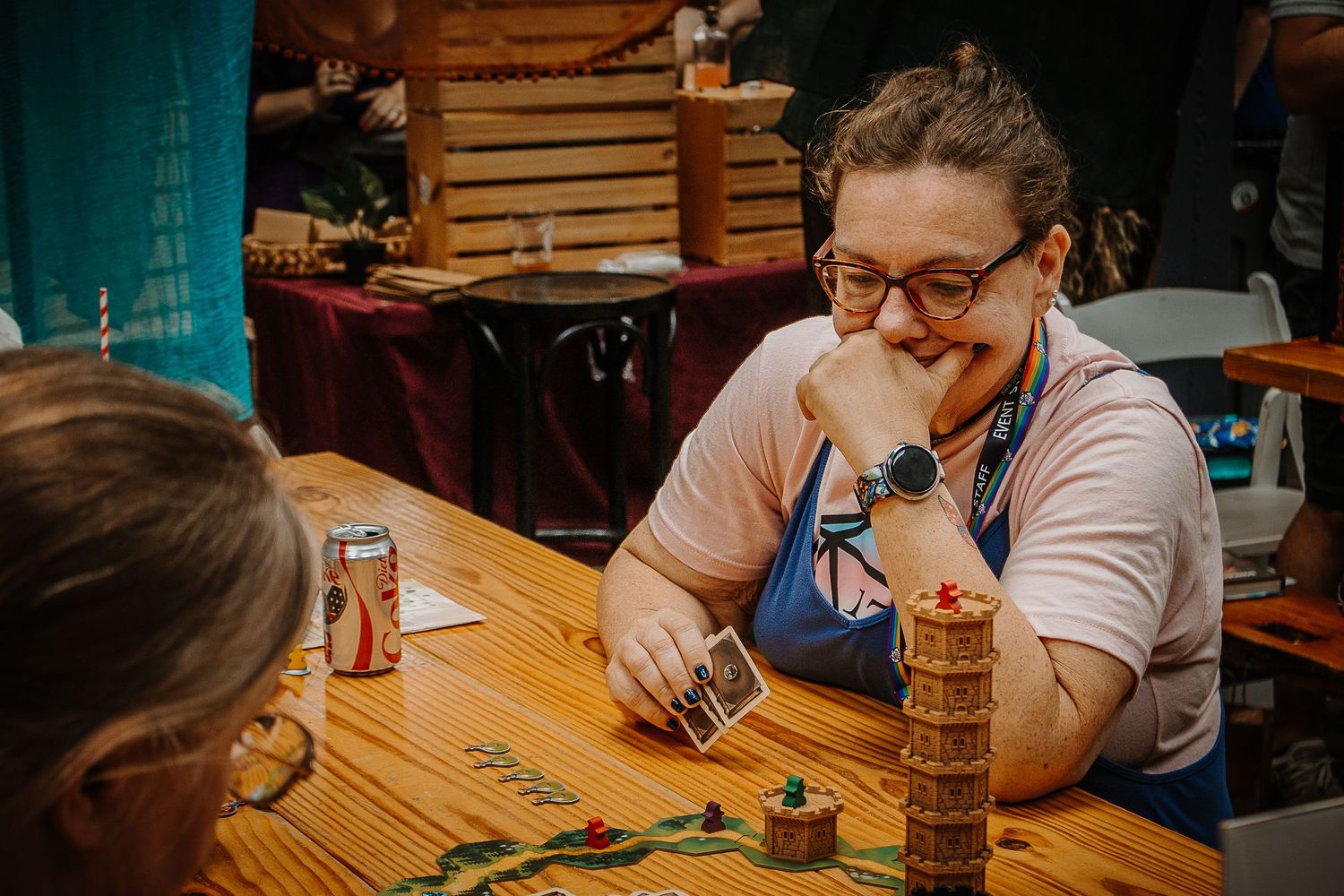 A smiling woman plays a card game at a wooden table during a tabletop gaming event.
