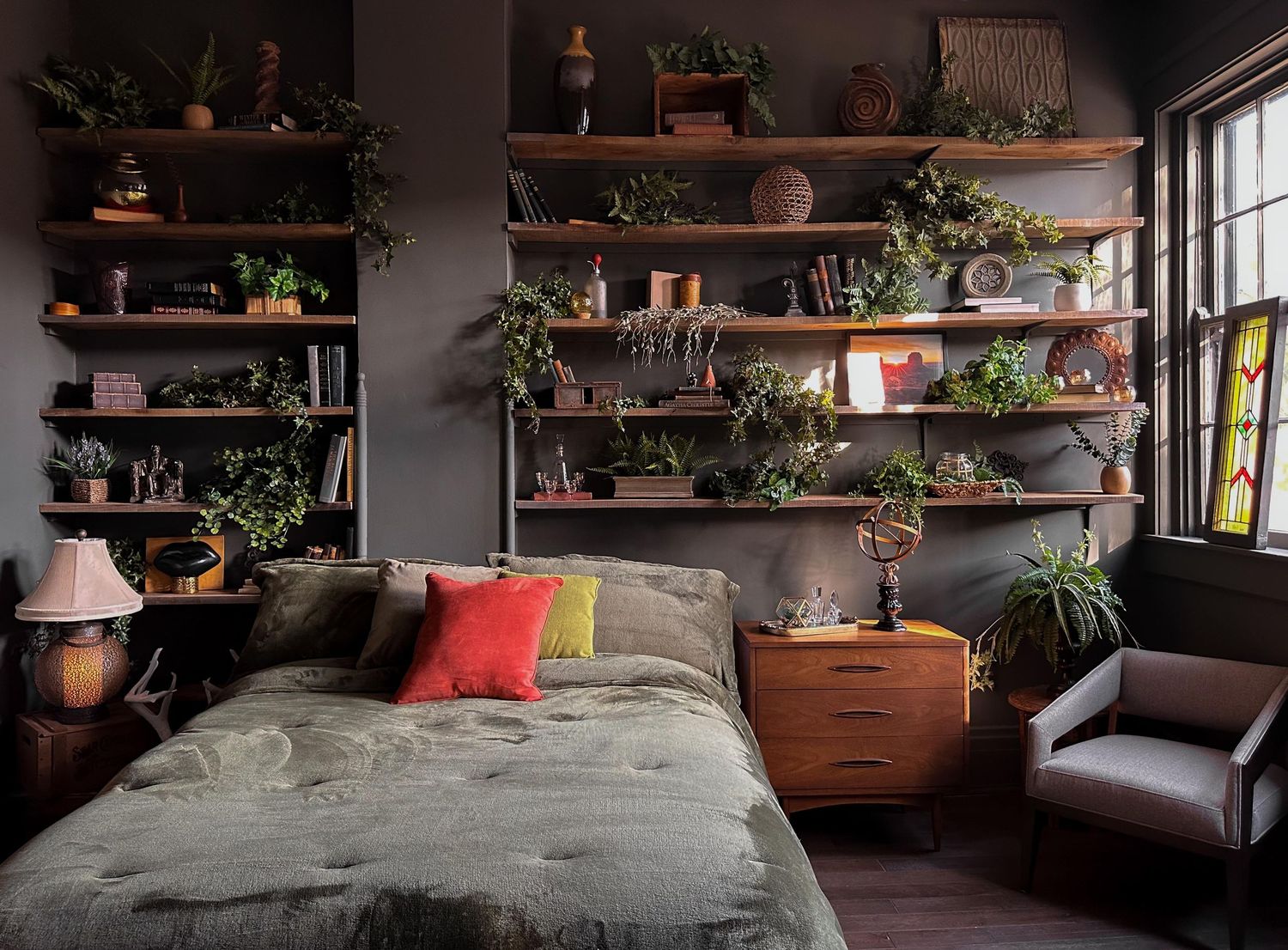 Cozy bedroom with wooden shelves filled with lush green plants above a bed with colorful pillows.