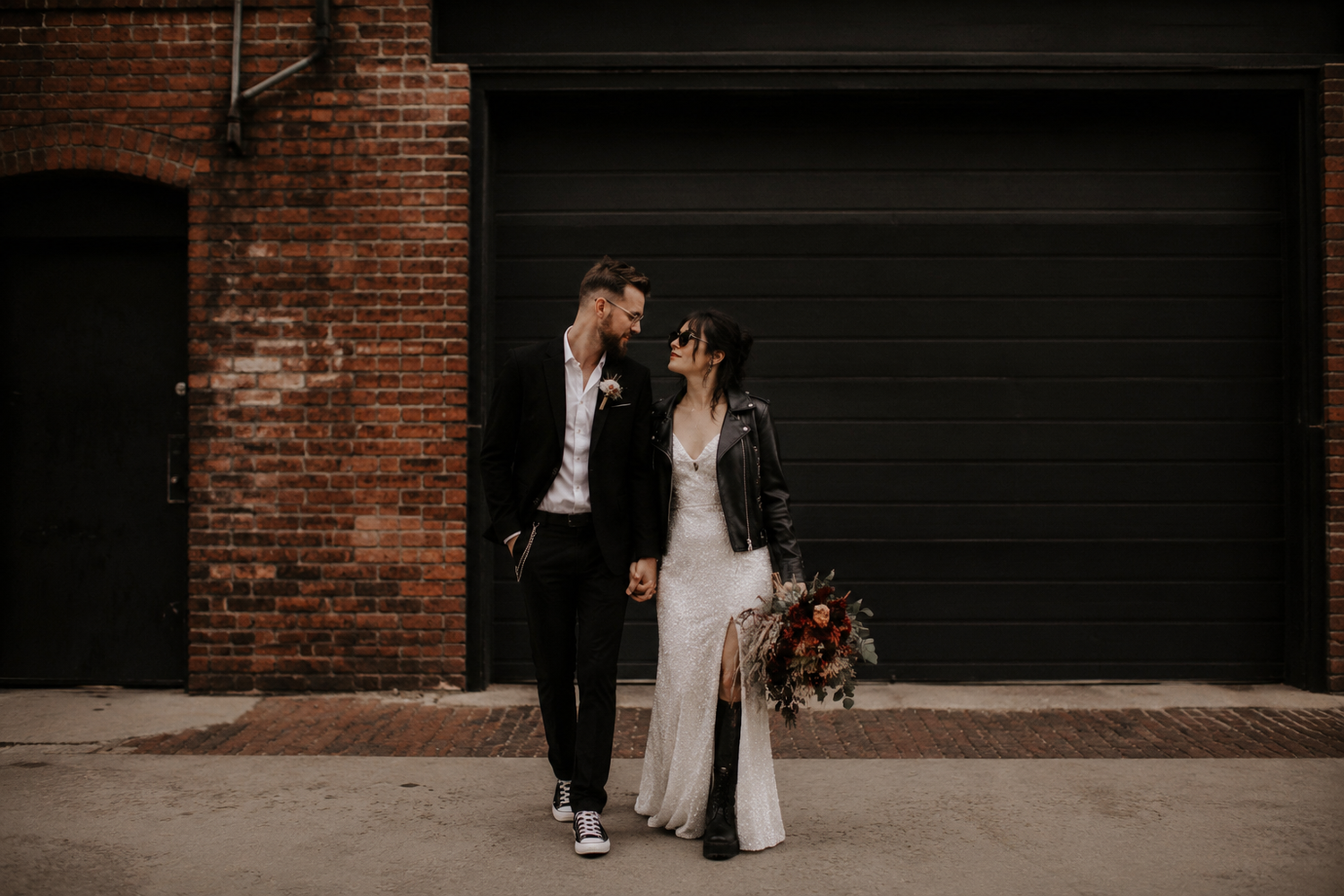 Bride and groom sharing a romantic moment in an urban alley with brick wall backdrop.