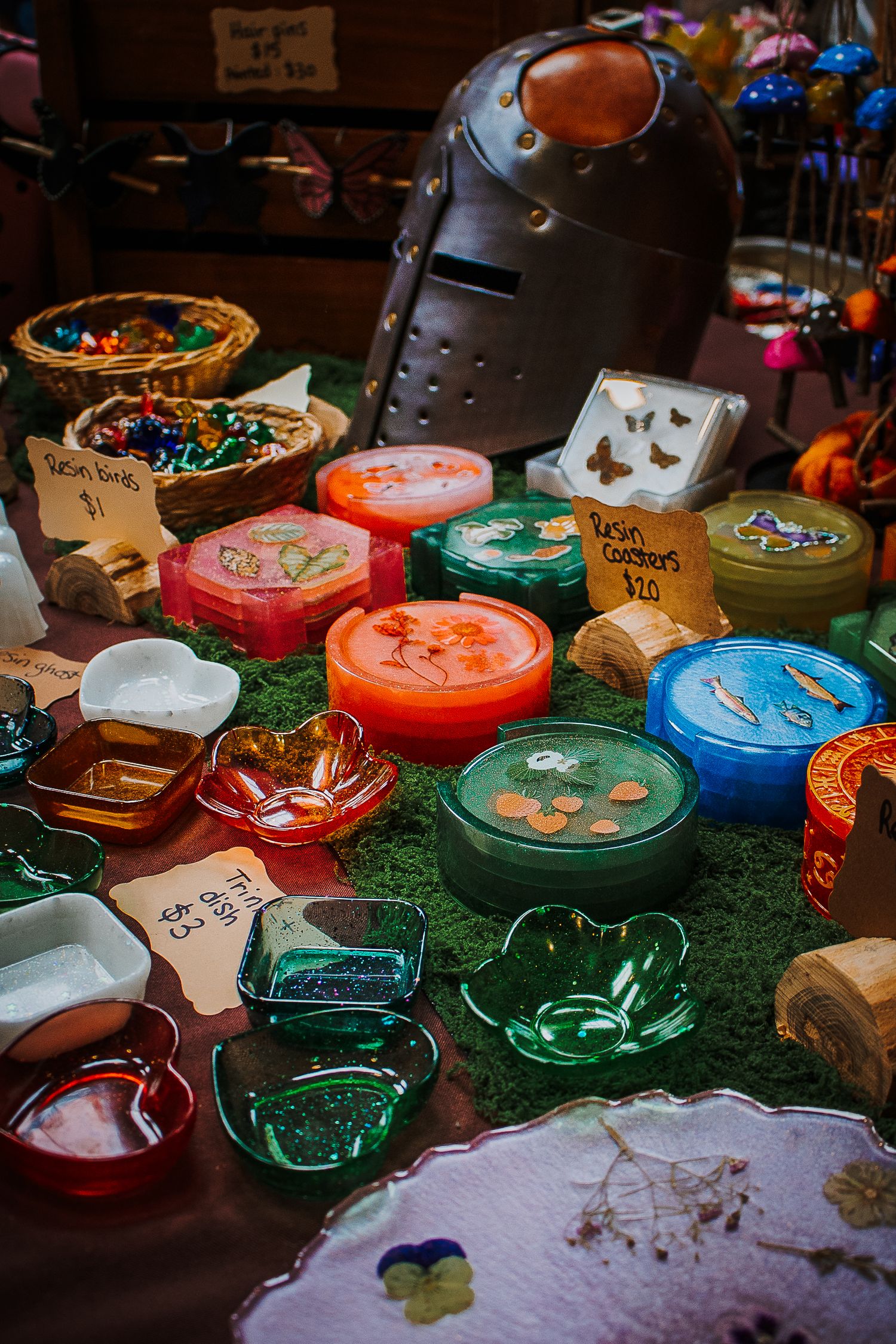 Colorful handmade resin coasters, rings, and decorative items displayed on a moss-covered table at a craft fair.