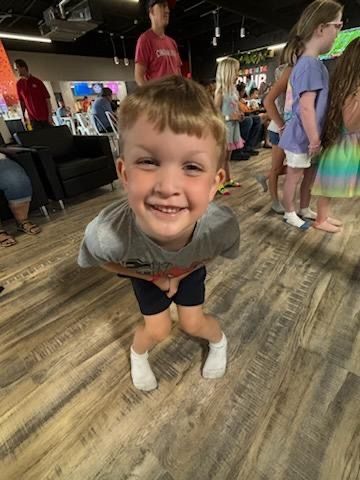 Happy toddler boy smiling and leaning forward playfully indoors at a fun family entertainment venue.