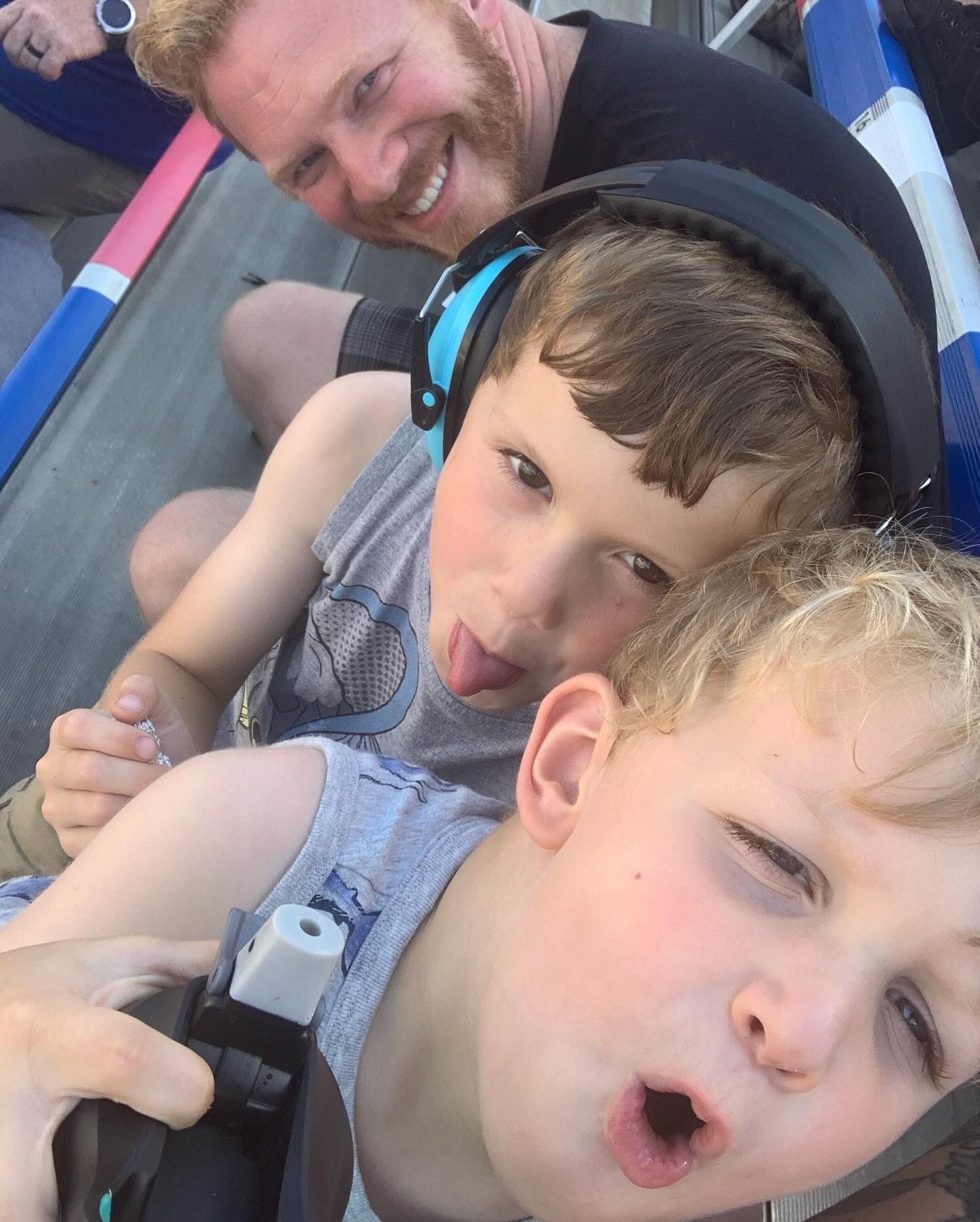 Father smiling with two young boys making funny faces on amusement ride.