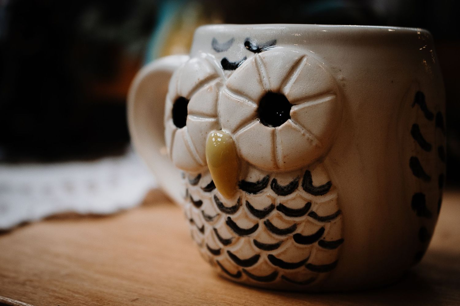 Cute ceramic owl-shaped coffee mug on a wooden surface.