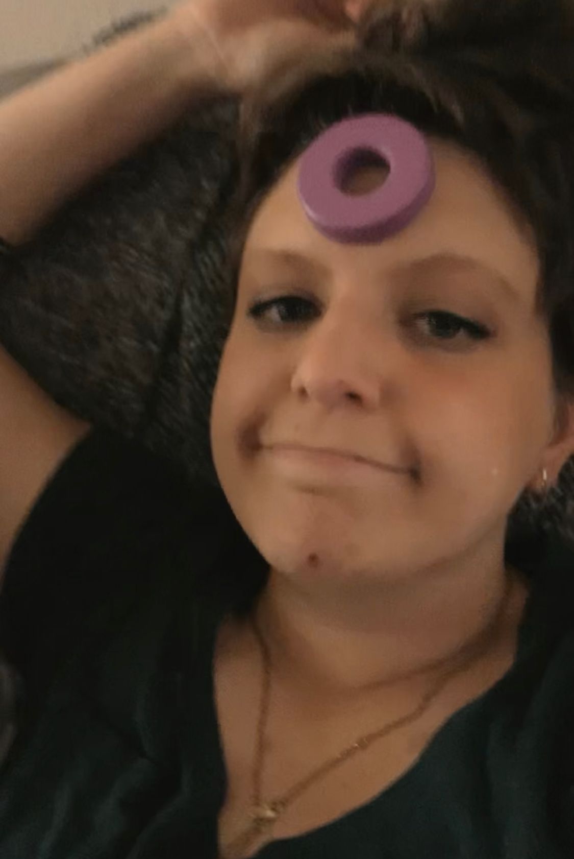 Woman smiling with purple ring toy balanced on forehead indoors.