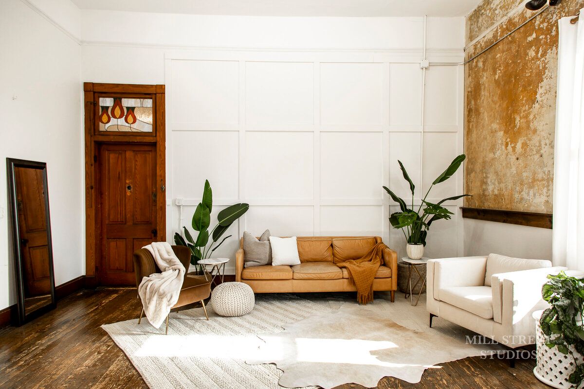 Boho living room with caramel leather sofa, white armchair, tropical plants, and cowhide rug.