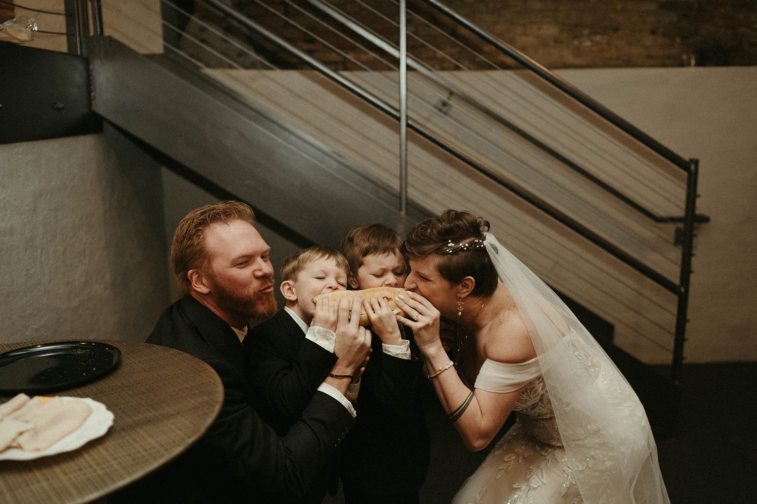 Bride and groom kissing young boy on cheeks at wedding reception table.