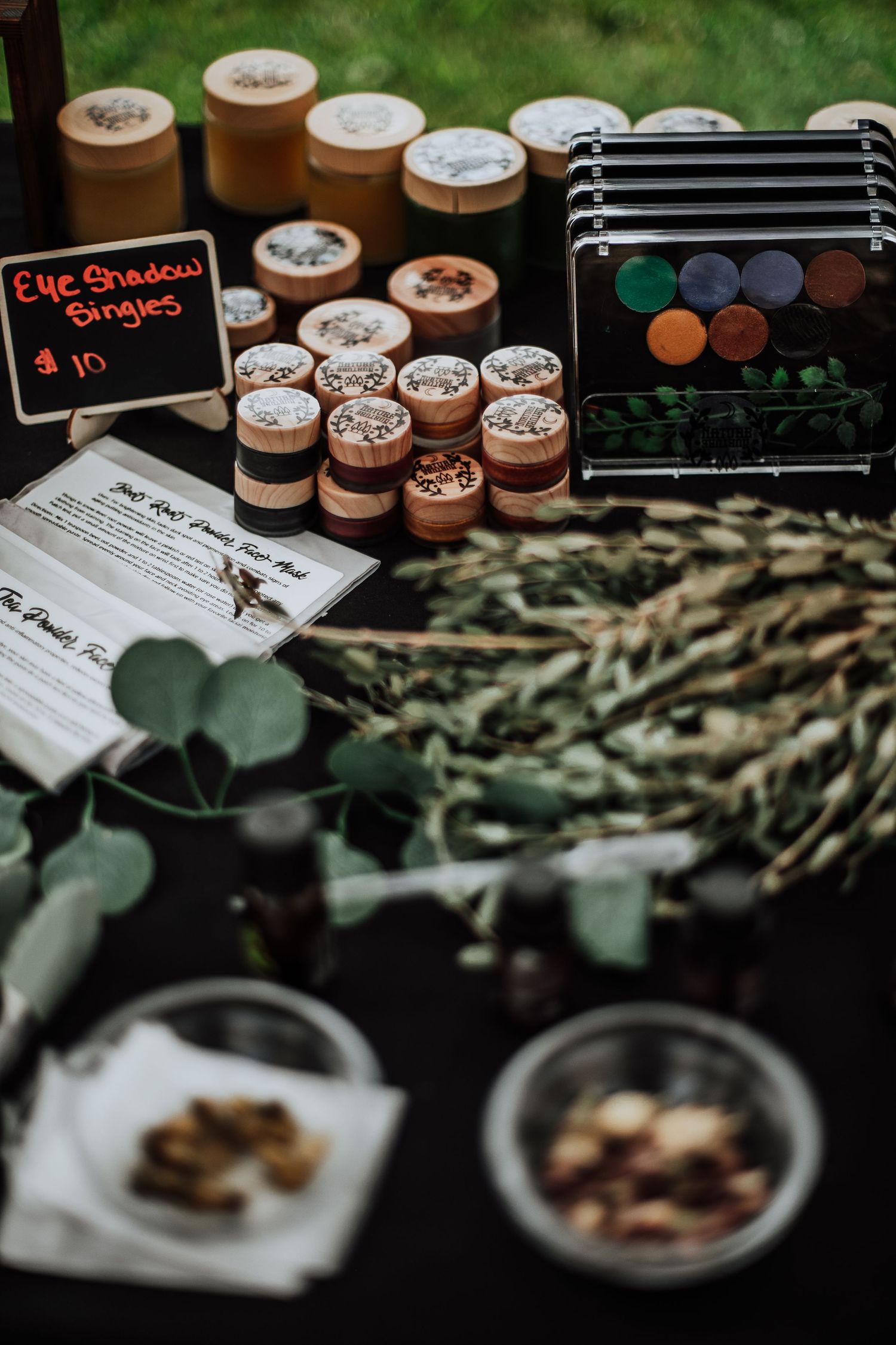 Eye shadow singles displayed at a craft market booth with eucalyptus decor.