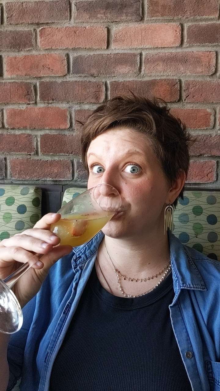 Woman making a funny face while sipping a cocktail in a martini glass at a brick wall bar.