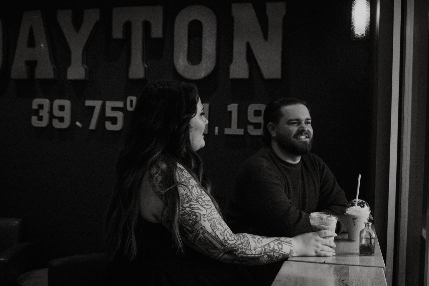 Black and white photo of a tattooed couple sharing drinks at a Dayton cafe.
