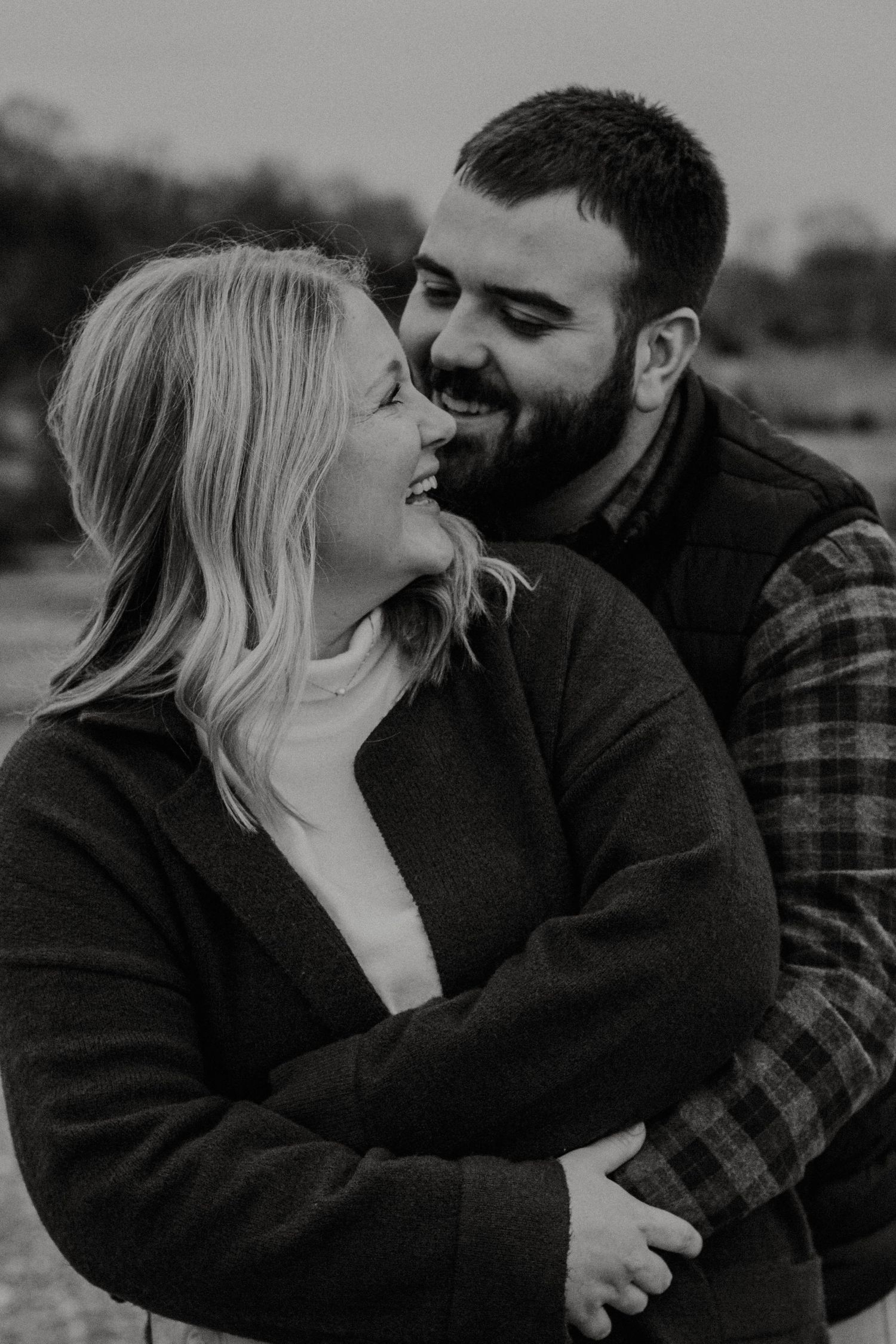 Black and white photo of bearded man embracing laughing blonde woman outdoors.
