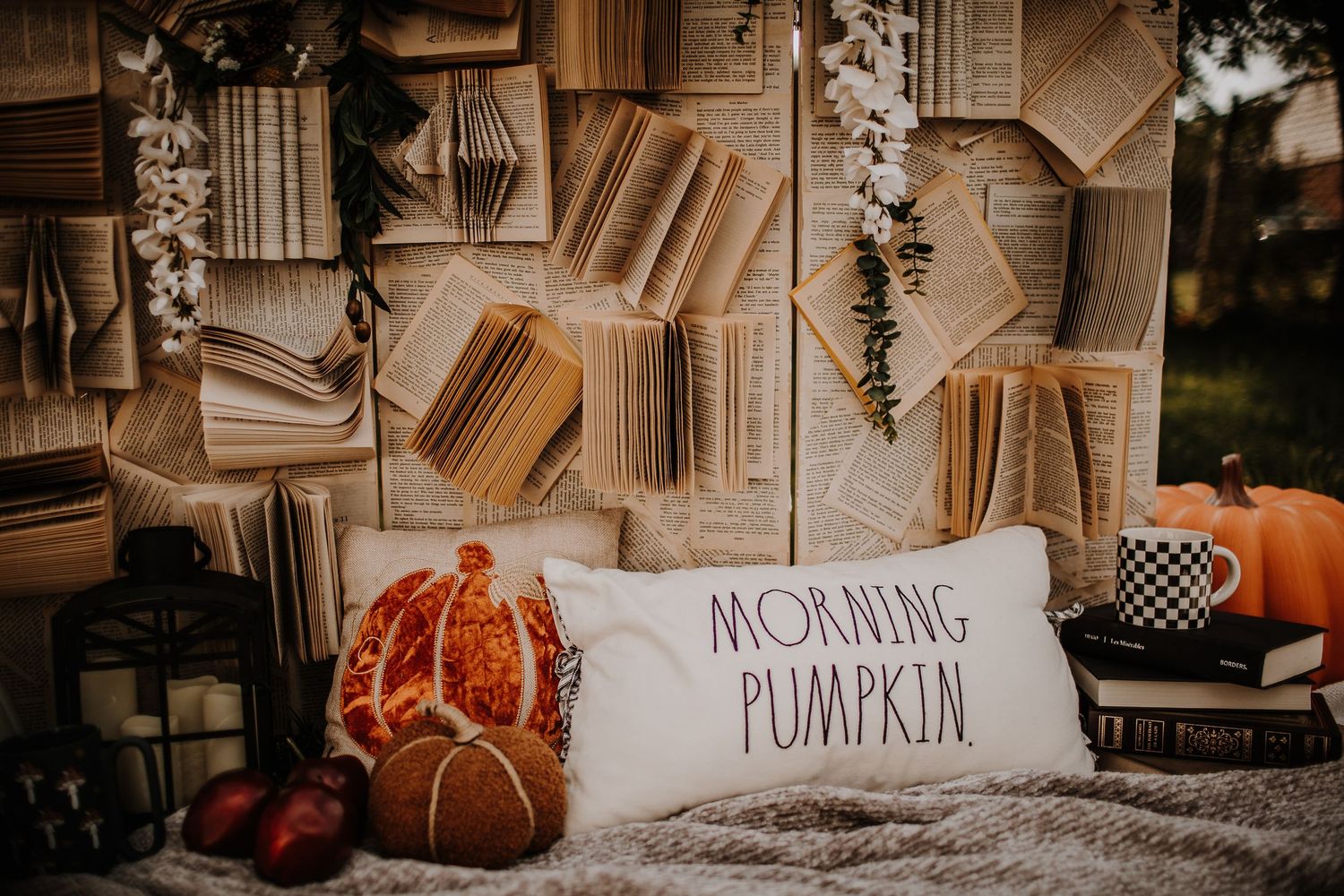 Cozy fall display with open books wall, Morning Pumpkin pillow, pumpkins, and autumn decor on a soft blanket.