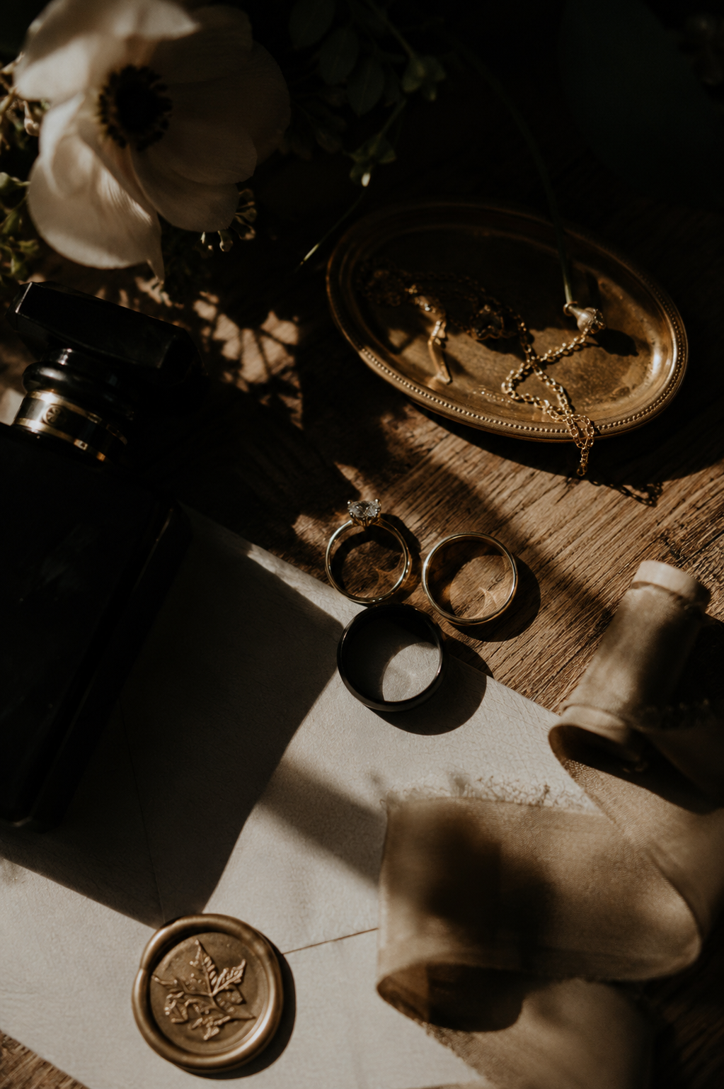 Flat lay of gold wedding accessories including rings, jewelry, wax seal, and flask in warm moody lighting.