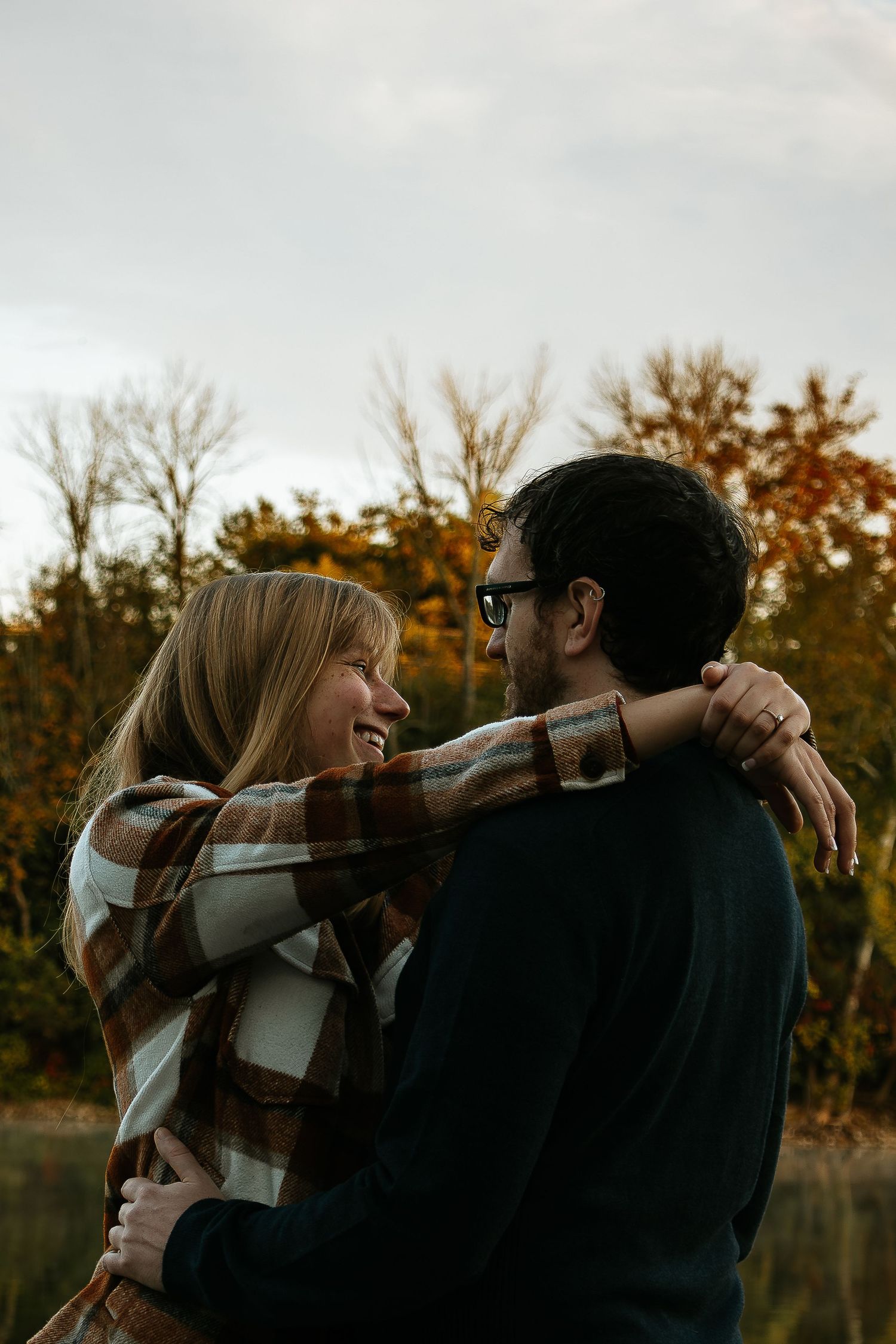 A smiling couple embraces warmly outdoors surrounded by colorful autumn foliage.